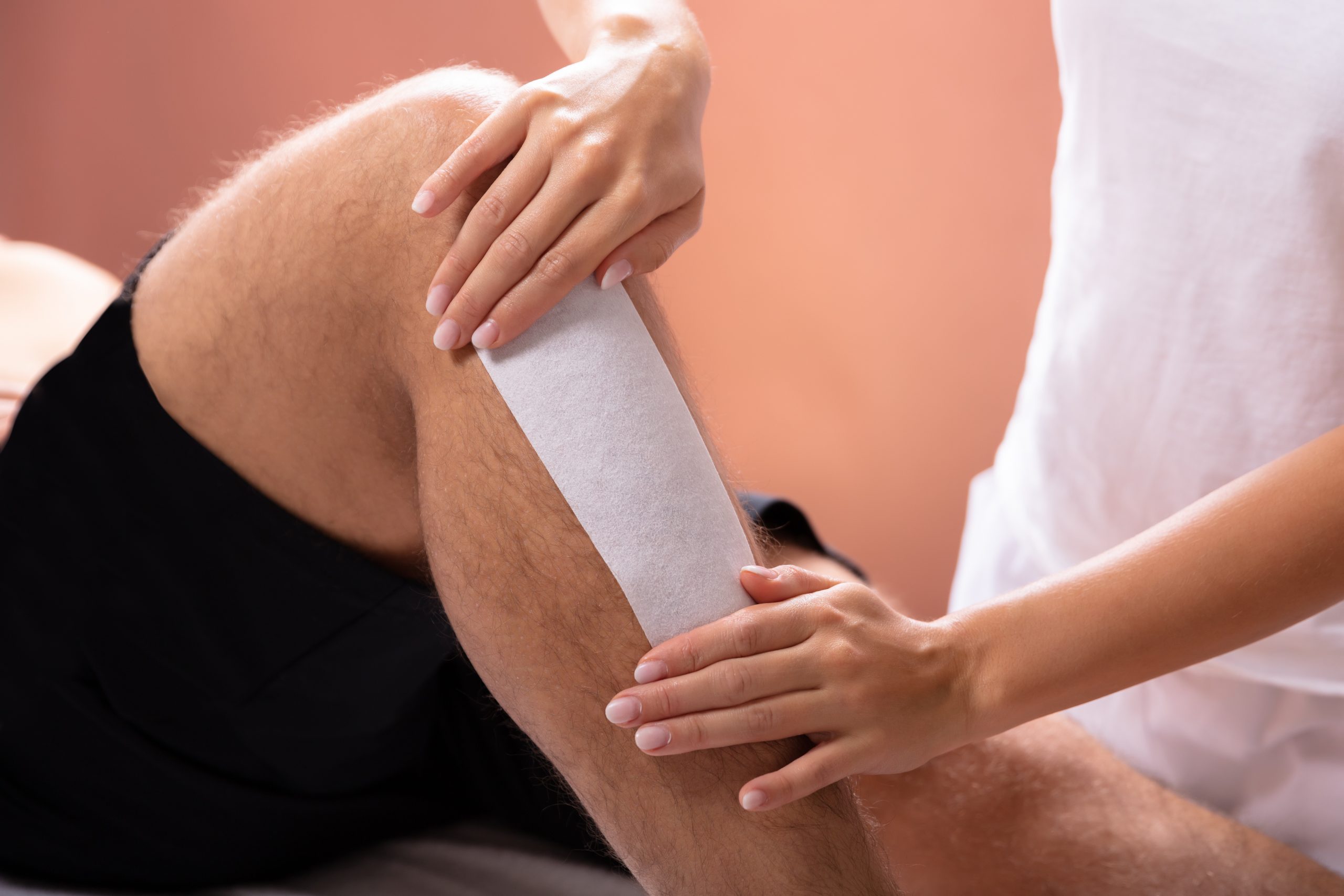 Close-up Of Therapist Hand Waxing Man's Leg With Wax Strip